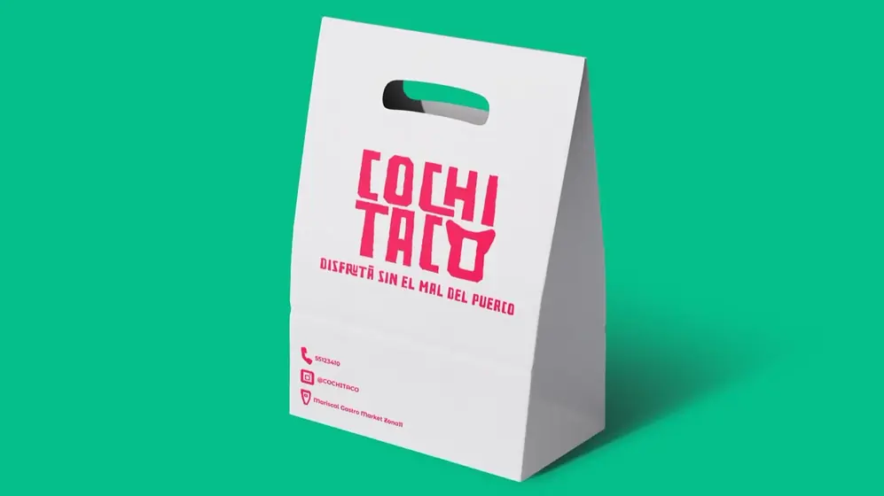 Bolsa de papel blanca con asa troquelada, logo rosa de Cochitaco y datos de contacto al pie, sobre fondo verde